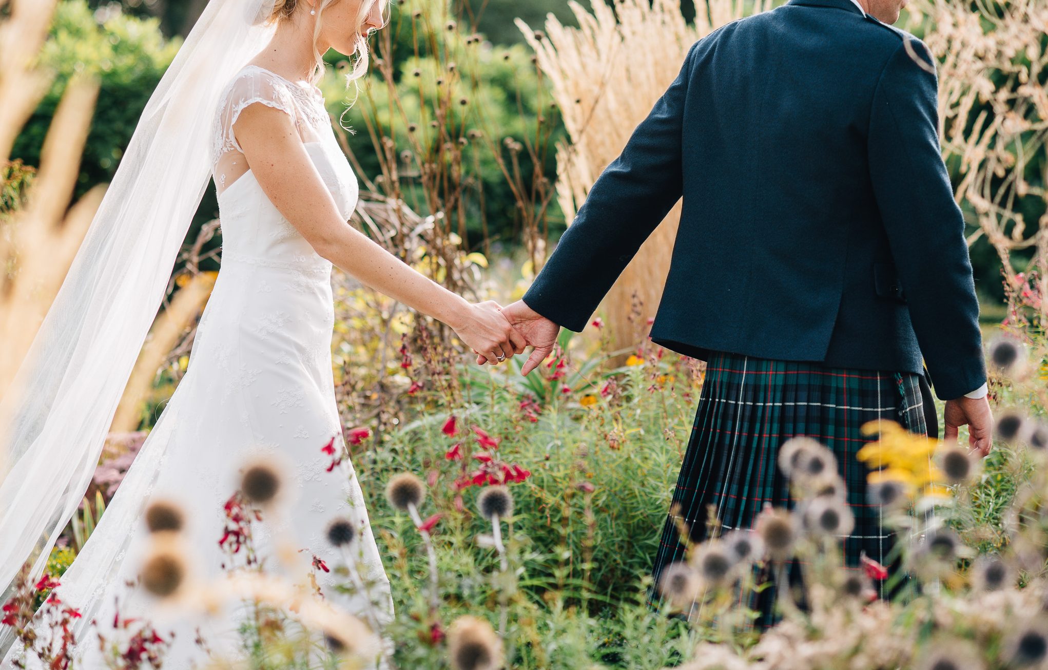 bride and groom hand in hand walking through a garden