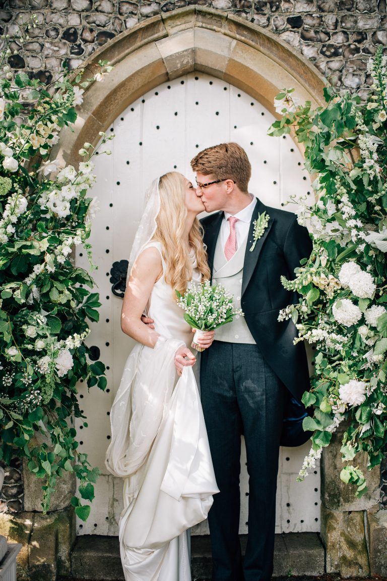 bride and groom kissing outside church doors surrounded by greenery and white flowers